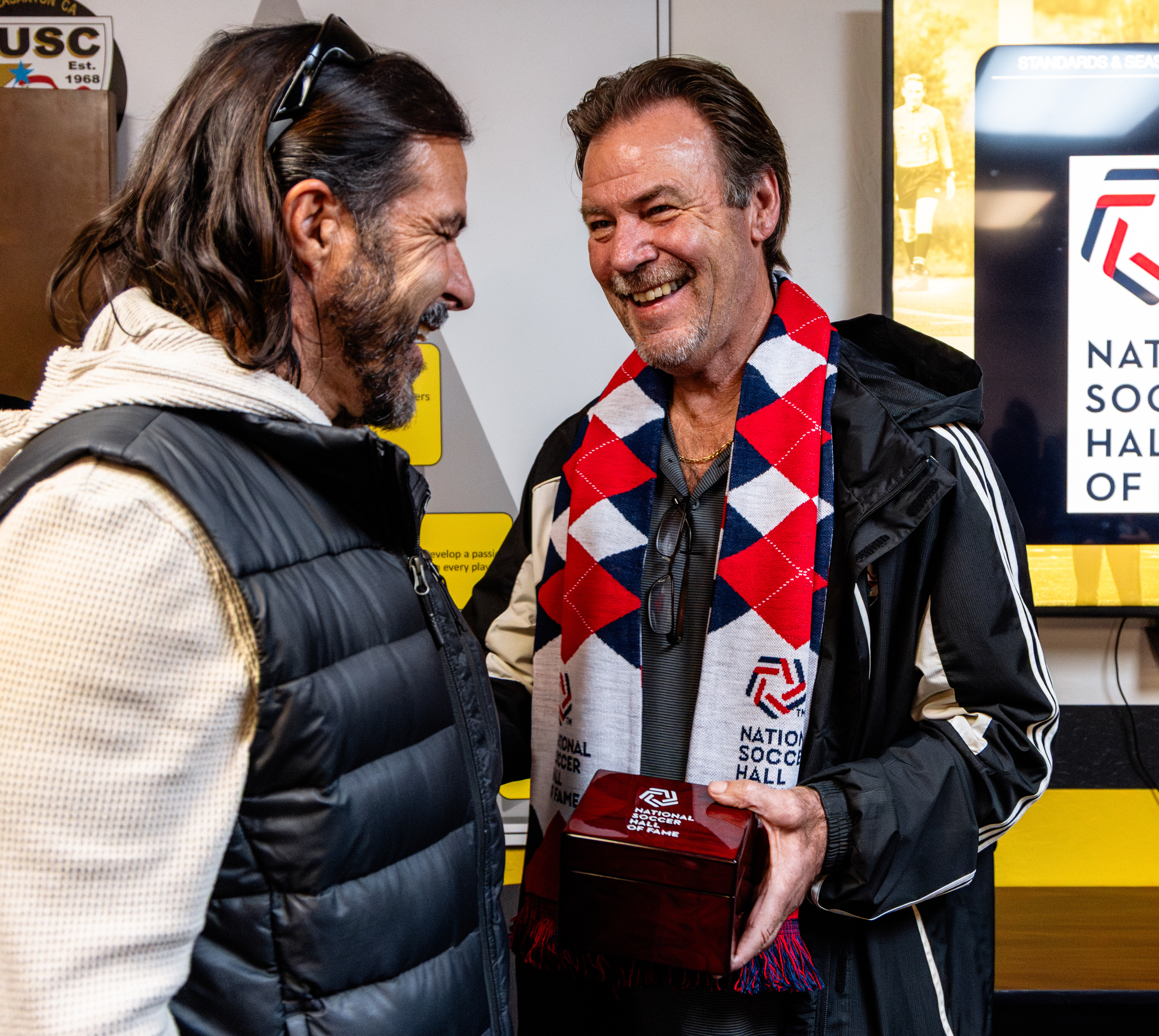 Two men, one of whom is wearing a red, white and blue scarf.