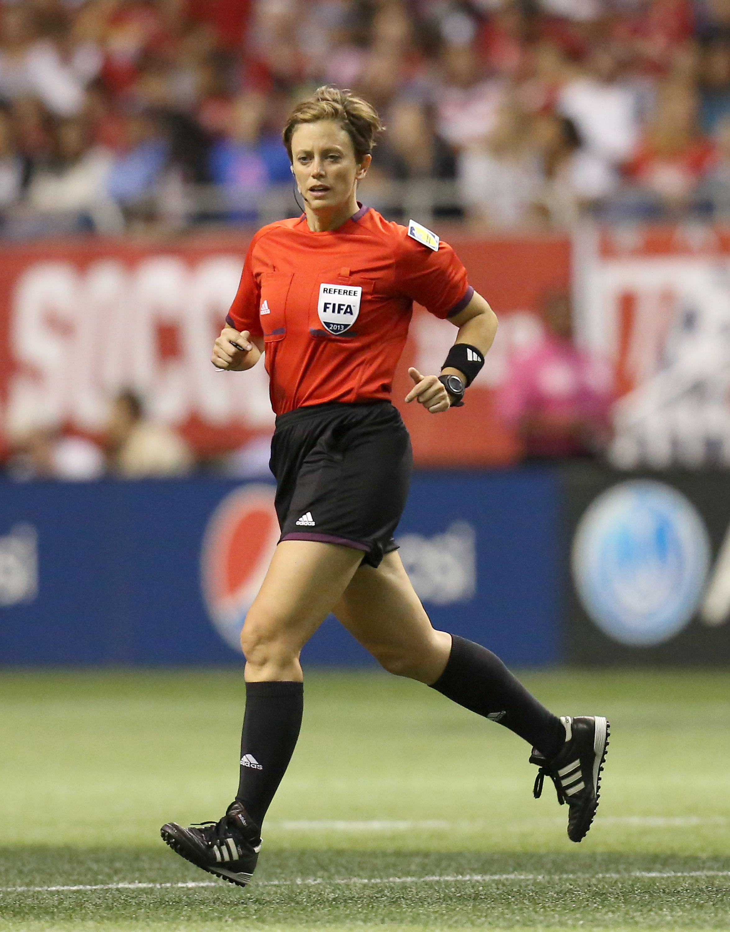 A soccer referee (Kari Seitz) running during a match in a red jersey.